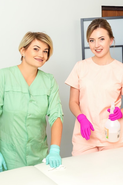 Two medical workers disinfect the patient's couch with sanitizer spray and a clean napkin Health and hygiene concept