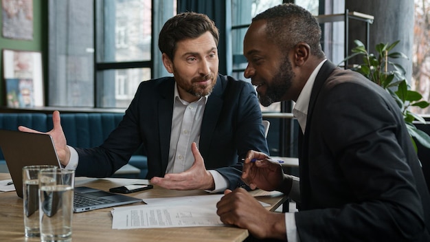 Two men amazed diverse workers with laptop in office talking emotional discuss project startup