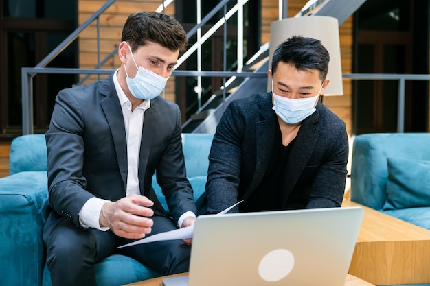 Two men are discussing the plan on a laptop Protected against COVID 19 with a protective mask