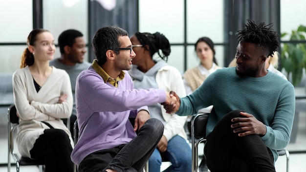 Two men communicate while sitting on a chair waiting for a speaker