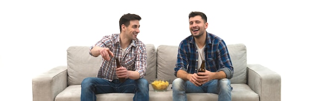 The two men drink a beer with chips on the sofa on a white wall background