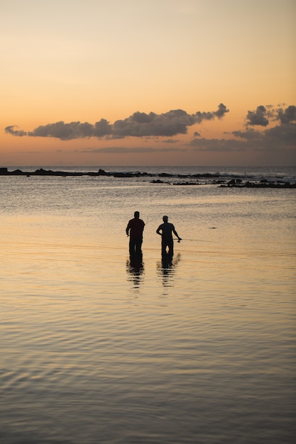 Two men fishing in the ocean from the beach at sunset