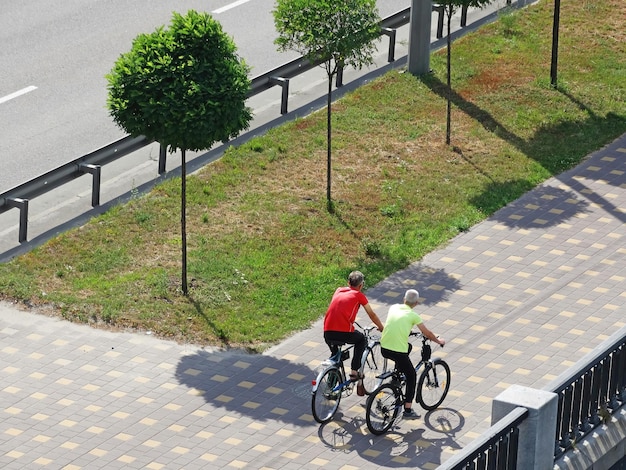 Two men riding a sport bikes down the street among beautifully trimmed trees view from above from the back Sports in the city Active men in sport clothing riding bikes