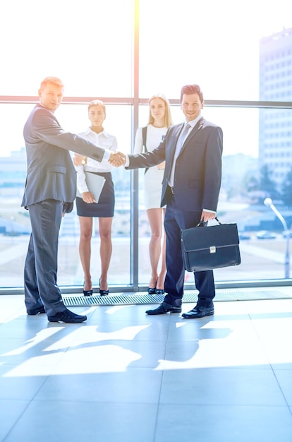 Two men shaking hands with one wearing a suit and the other wearing a briefcase.