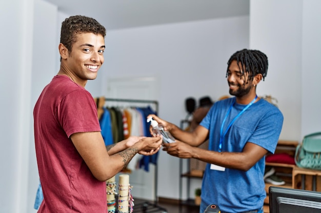 Two men shopkeeper and customer cleaning hands using sanitizer gel at clothing store