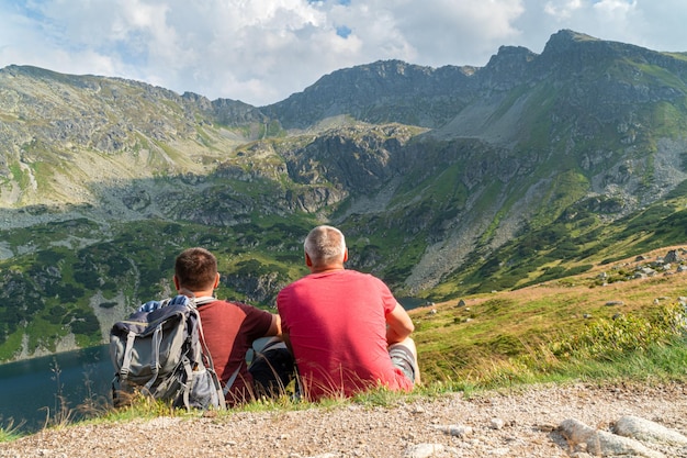 two men sitting on the ground look into the distance at a beautiful view of the mountains