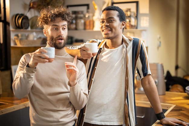 Two men talking and drinking coffee on kitchen at home