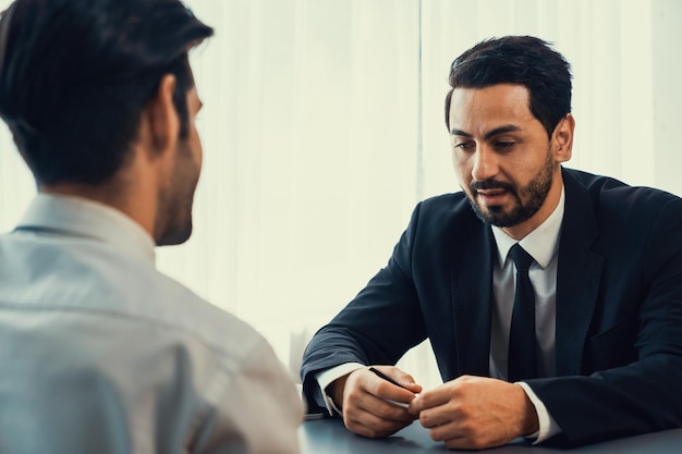 Two men talking at a table, one of them is wearing a suit and the other is wearing a tie.