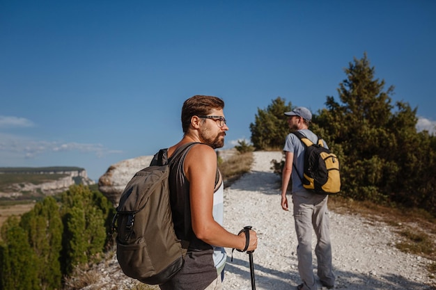 Two Men walking on rocky slope carrying Backpacks using trekking Sticks