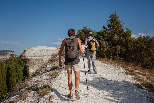 Two Men walking on rocky slope carrying Backpacks using trekking Sticks