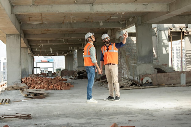 Photo two men wearing orange vests are standing in a construction site