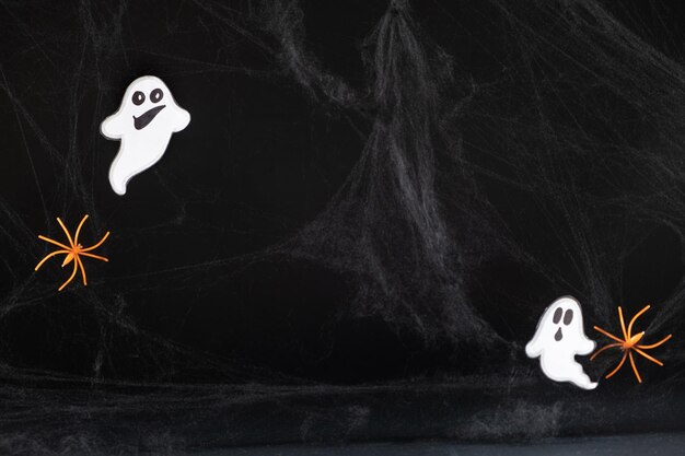 Photo two merry ghosts made of paper on a black background with spider webs and spiders with space for text in the middle