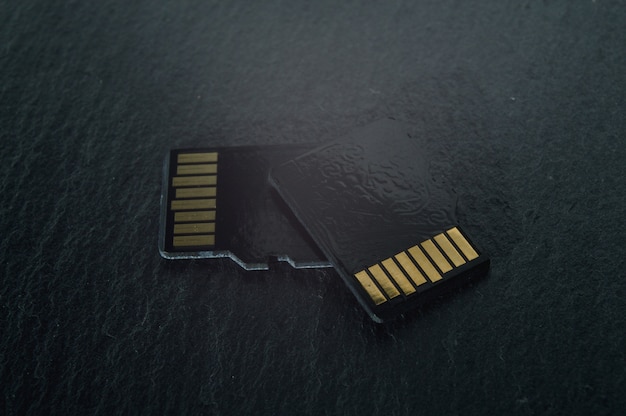 Two micro sd cards lie on top of each other on a dark textured background, with golden contacts at the top. close-up.