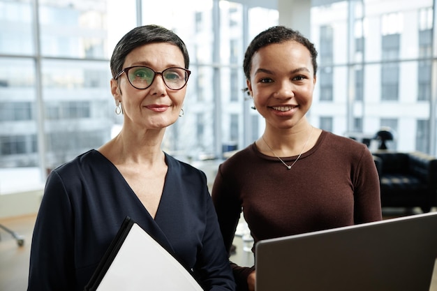 Two modern businesswomen smiling at camera in office interior