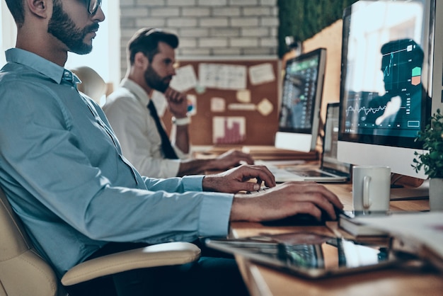 Two modern men in formalwear working using computers while sitting in the office