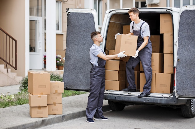 Photo two movers wearing uniforms are unloading the van full of boxes house move mover service