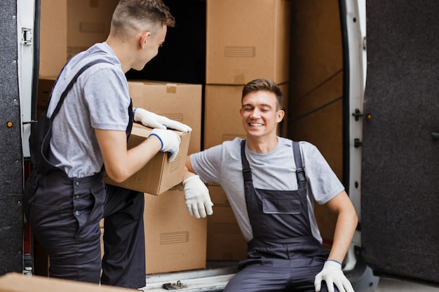 Two movers wearing uniforms are unloading the van full of boxes House move mover service