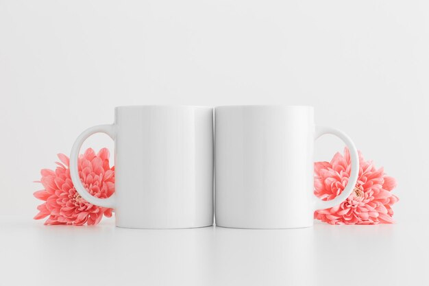 Photo two mugs mockup with pink chrysanthemums on a white table