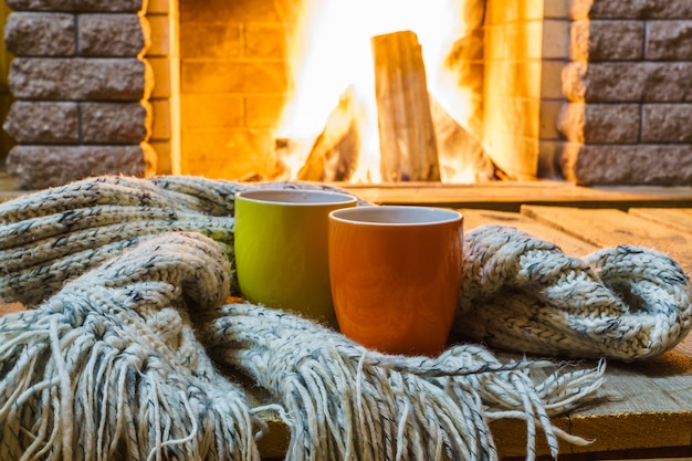 Two mugs tea or coffee, wool things near cozy fireplace, country house, winter