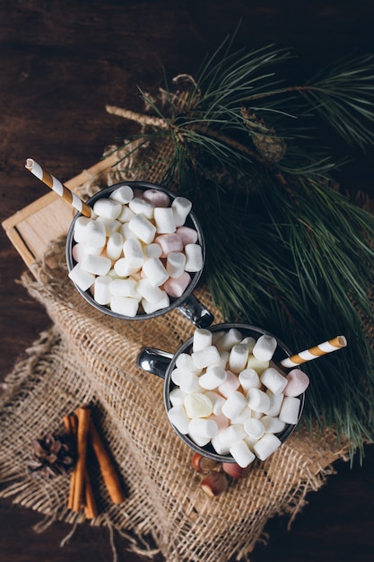 Two mugs with cocoa and marshmallows on a brown background