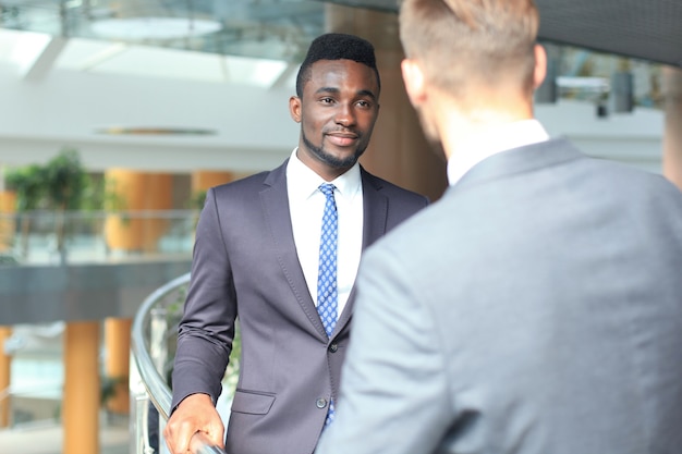 Two multinational young businessmen discussing business at meeting in office.