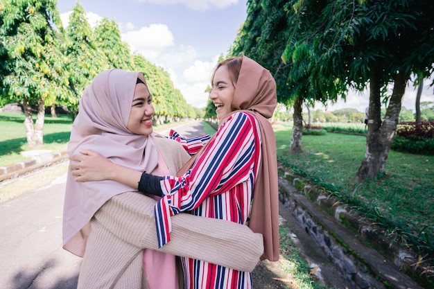 Two muslim girls hug on the sidewalk. Feel joyfull and happy together.