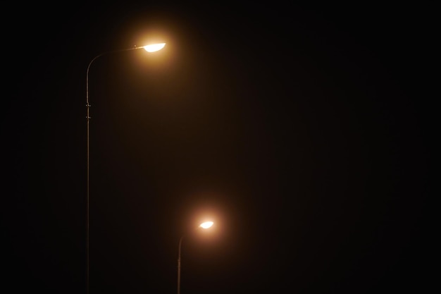 Two night lamppost shines with faint mysterious yellow light through evening fog at quiet night