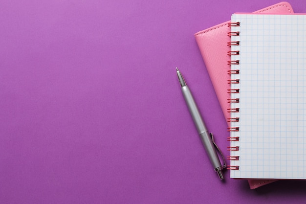 Two notebook and pen on a bright purple background. top view. office tools. space for text