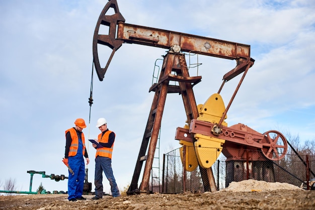 Two oil men standing by petroleum pump jack