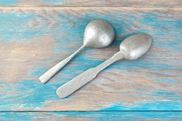 Two old aluminum spoons on blue wooden background. Copy space for text, food photography props.