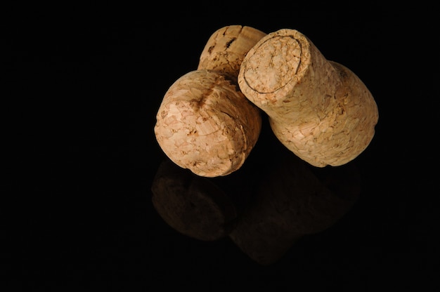 Two old wine corks on a black background with reflection