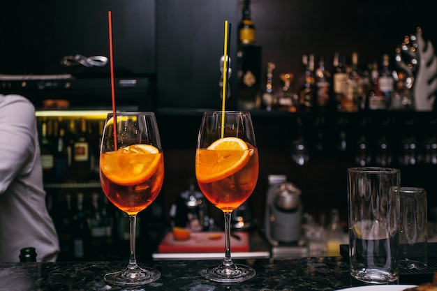 two orange alcoholic cocktails Aperol Spritz with cherries, orange zest on a dark background,