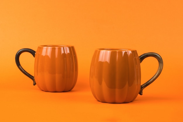 Two orange pumpkin-shaped mugs on an orange background. Pumpkin style.