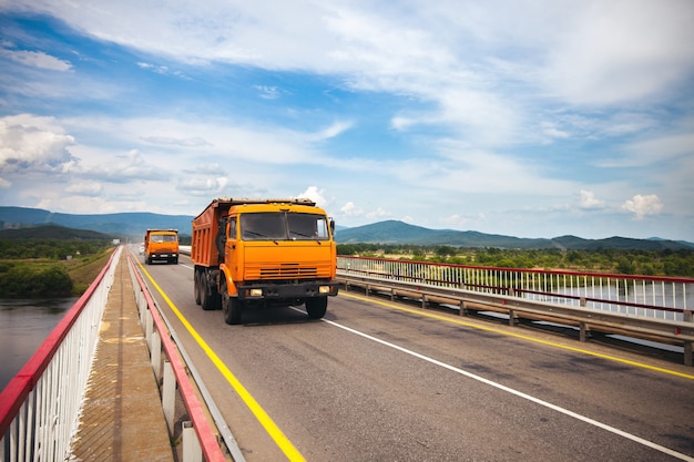 Two orange russian dump trucks moving over the bridge