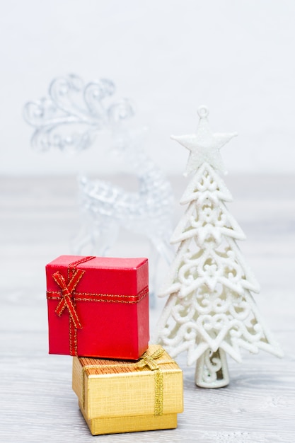 Two packaged gifts in boxes, Christmas white tree and deer on gray wooden background