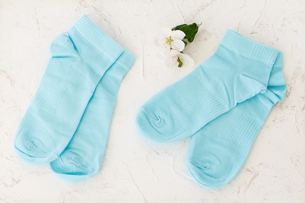 Two pair of blue women socks and flowers of an apple tree on the white structured background, Top view.