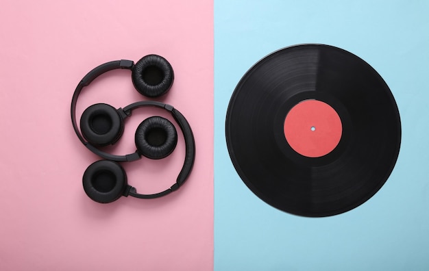 Two pairs of black stereo headphones and vinyl record on pink blue background