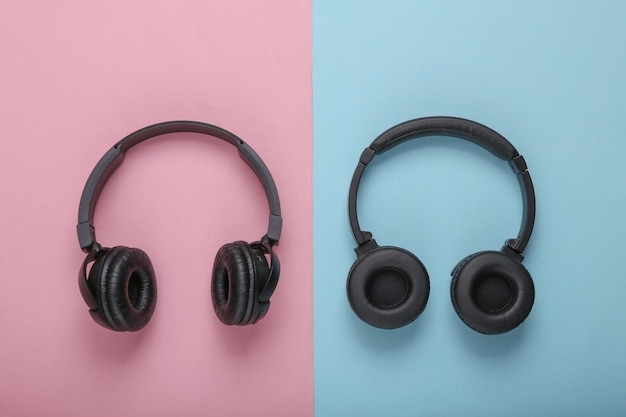 Two pairs of black wireless stereo headphones on a blue pink background