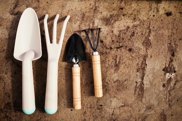 Two pairs of garden shovel and fork made up of white plastic wood and black metal on shabby brown background