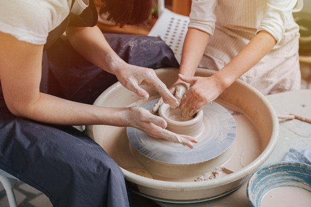 Two pairs of hands shaping clay vase on a pottery wheel in a workshop