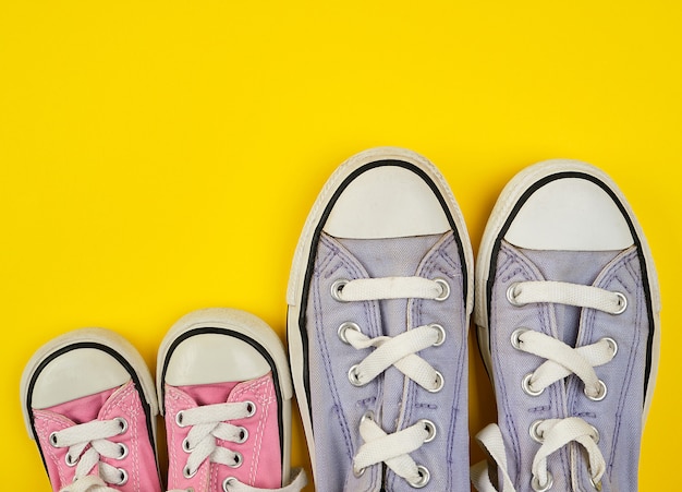 Two pairs of worn textile shoes of different sizes on a yellow background