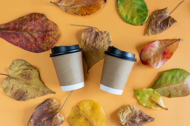 Two paper coffee cups with lids in autumn leaves with orange background