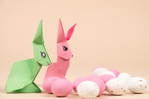 Two paper origami bunnies and an Easter egg on a beige background