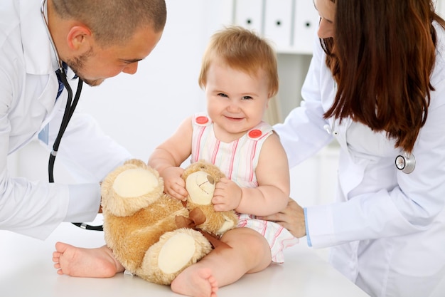 Photo two pediatricians are taking care of baby in hospital little girl is being examining by doctor with stethoscope health care insurance and help concept