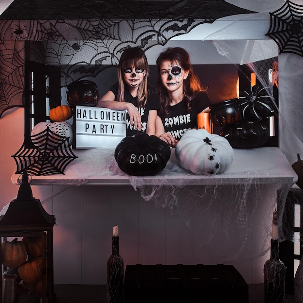 Two pensive girls with scary makeup are sitting next to traditionally decorated table.