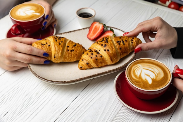 Two people eating a croissant and a cup of coffee.