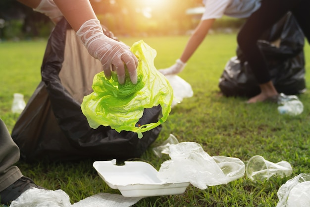 Two people keeping garbage plastic bottle into black bag at park in morning light