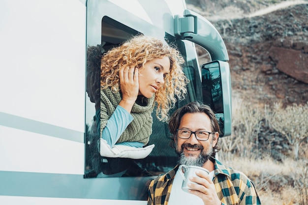 Two people man and woman enjoying travel road trip destination together Female looking outside her camper van and bearded male drinking coffee outdoor Off grid alternative house concept Van life