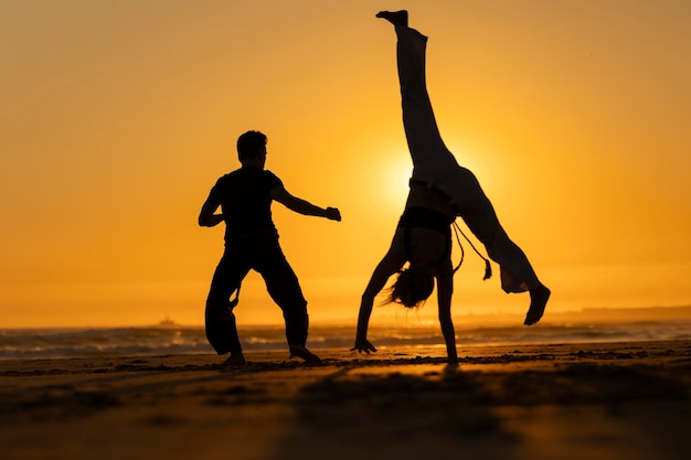 Photo two people practicing capoeira on the beach at sunset