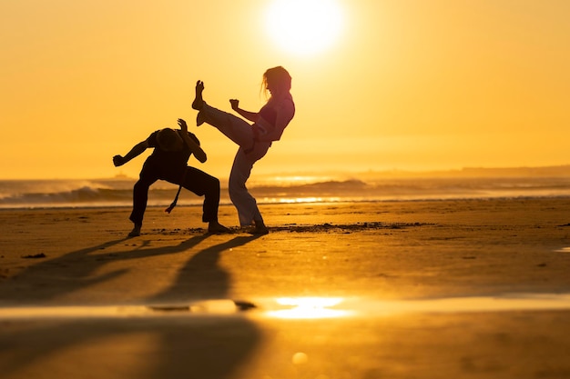 Photo two people practicing capoeira martial arts on the beach at sunset